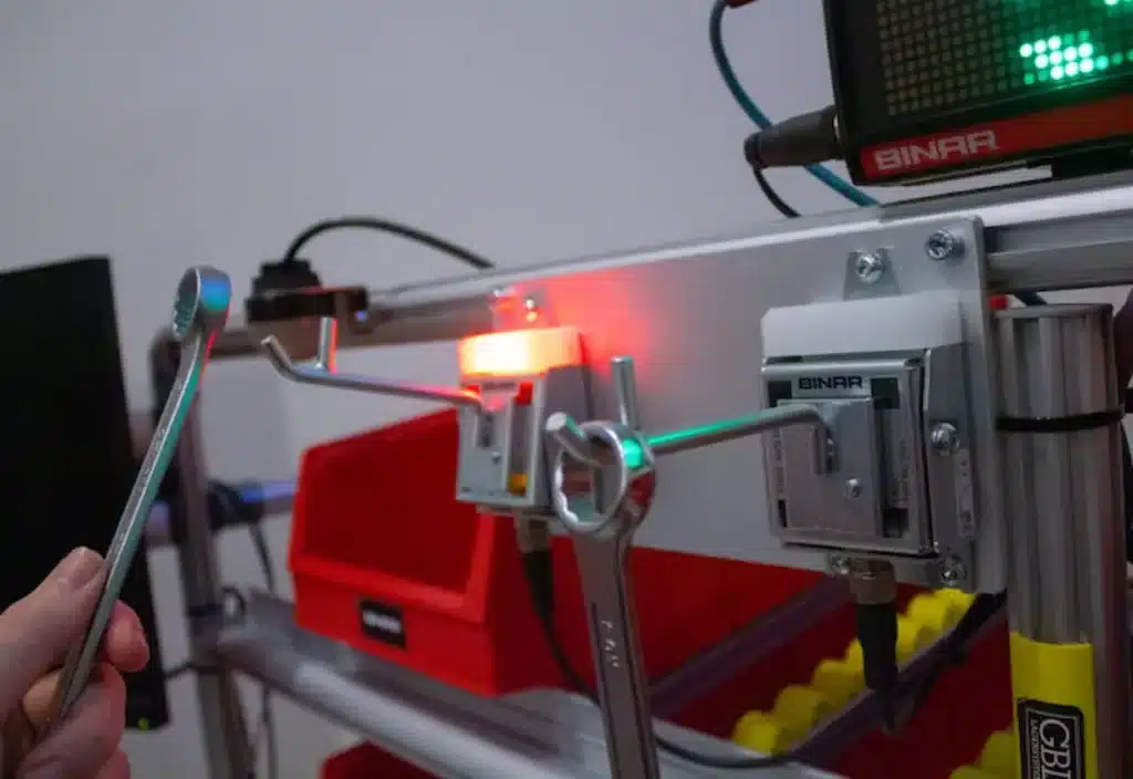Hand hanging a tool on an industrial workstation with a Binar LED display in the background
