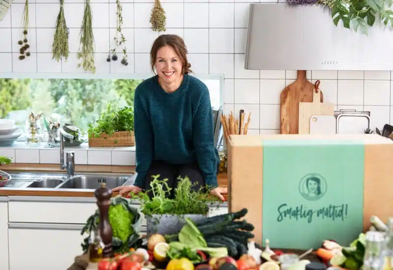 Woman sitting on kitchen counter with vegetables and a cardboard box in front of her