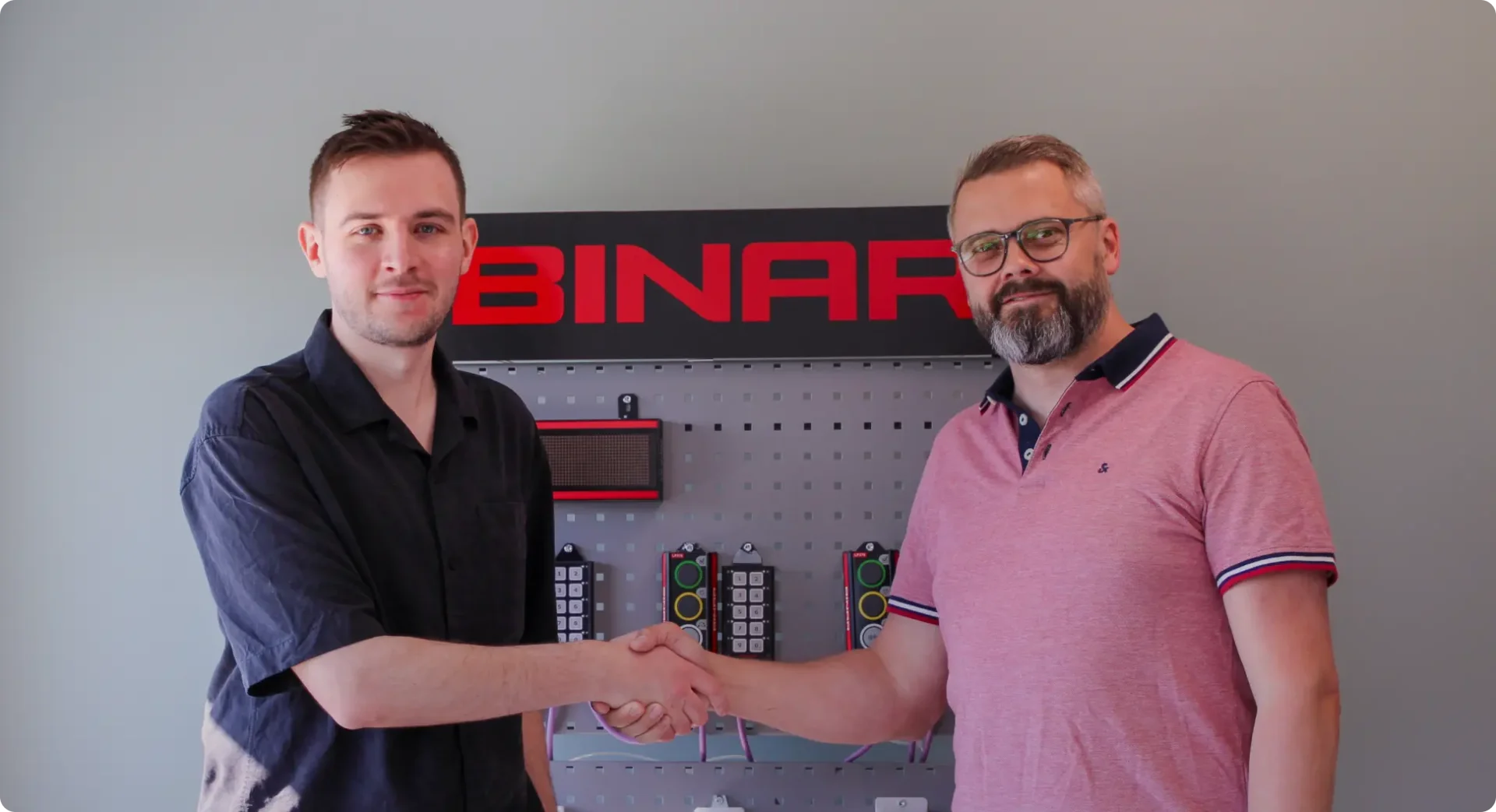Two men shaking hands in front of a Binar logo