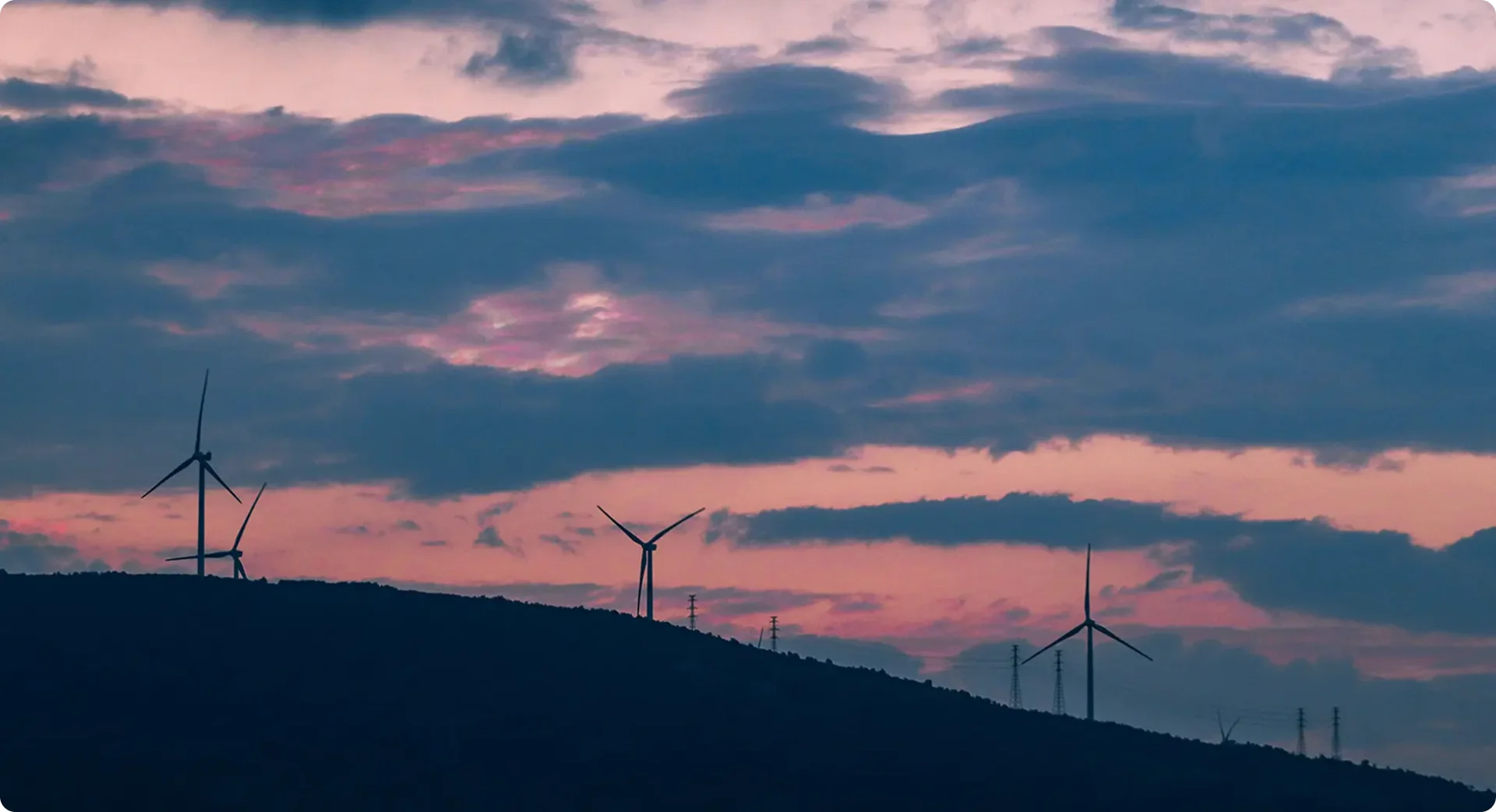 Windmills on a hill with a pink cloudy sky in the background