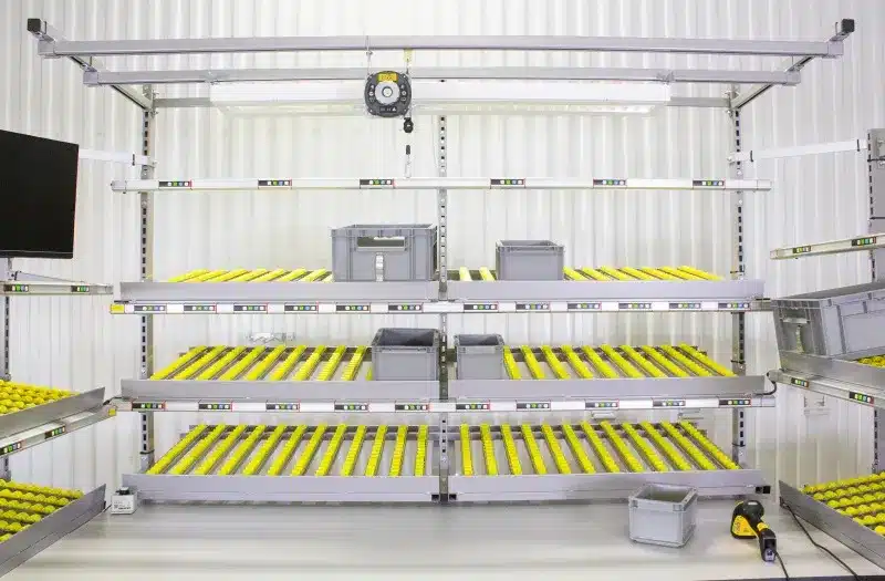 Modular industrial workstation with roller tracks, bins, a computer screen, and lighting